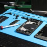 Close-up of disassembled smartphone parts on a blue repair mat with tools.
